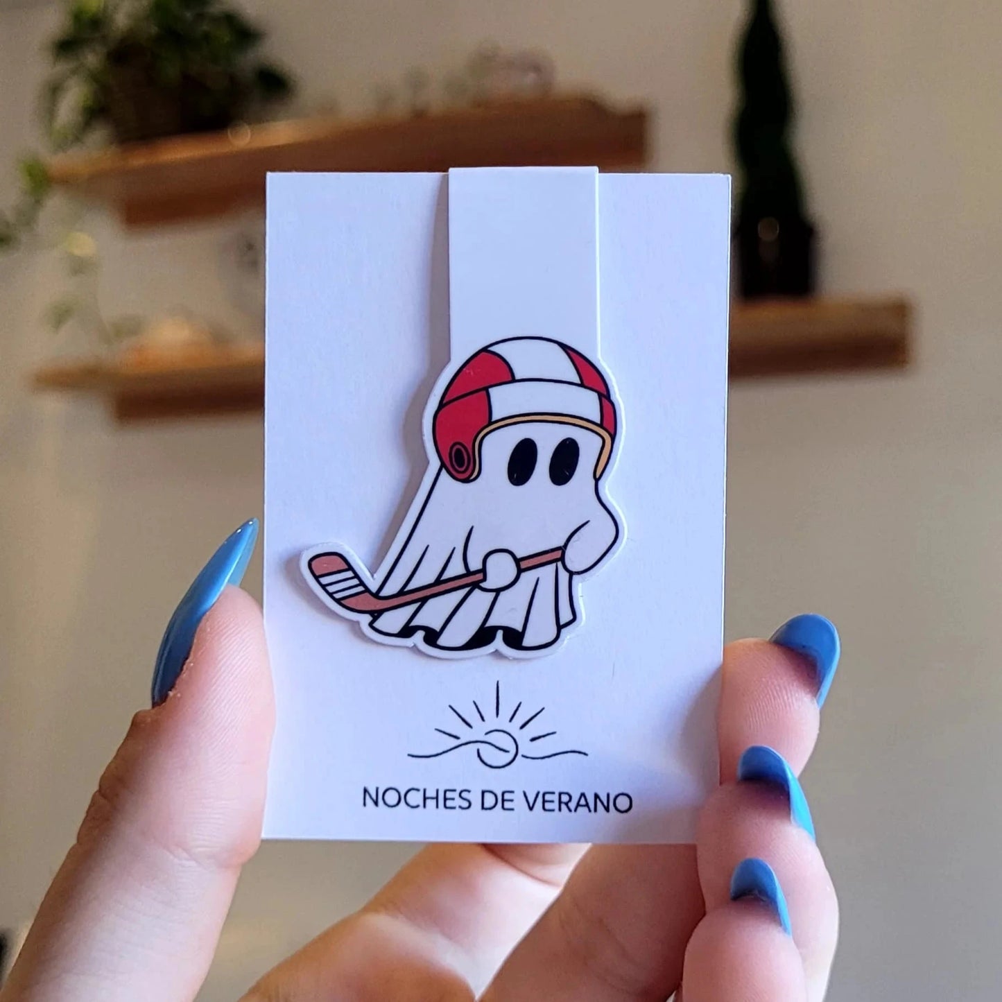 Marcapáginas magnético con diseño divertido de fantasma jugando al hockey con un casco rojo y un stick de hockey, perfecto para lectores que busquen un marcador de libros único y original de deportes.